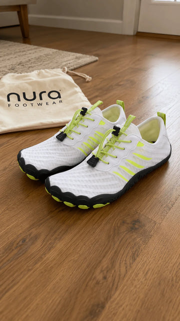 White sneakers with green accents on a wooden floor next to a Nura Footwear bag.